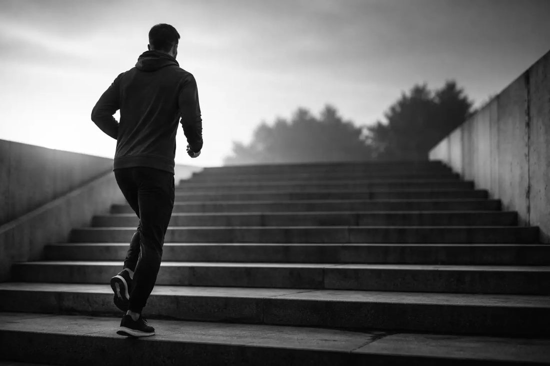 Homme en tenue sportive montant des marches, symbole de progression lente, constance et persévérance sur le long terme