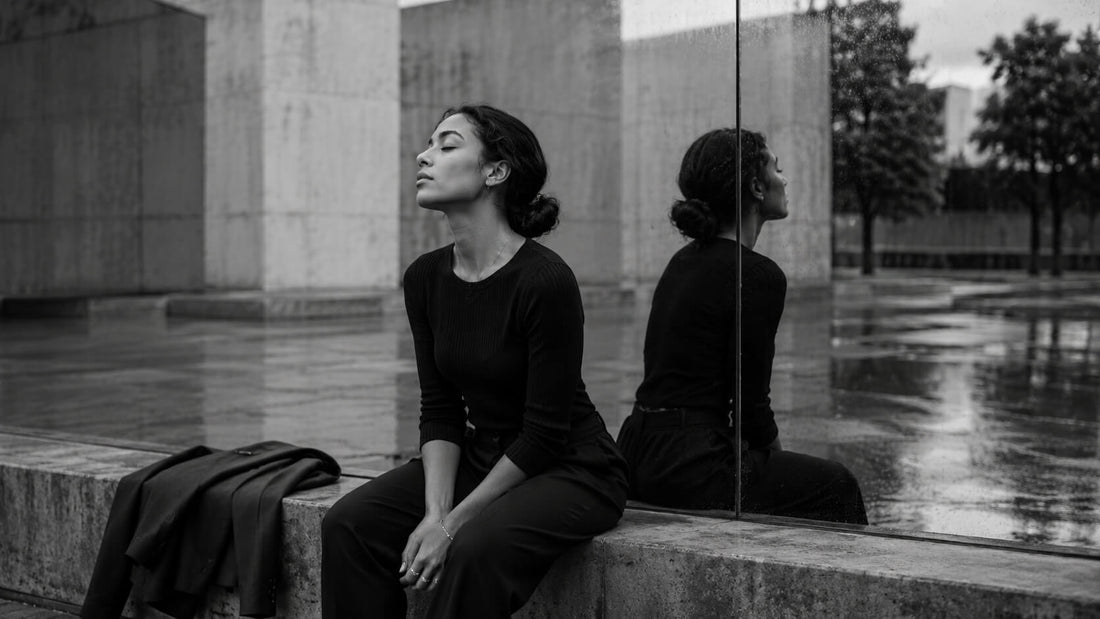 Femme assise face à son reflet dans un espace urbain en noir et blanc, symbole de la fatigue du personnage et du retour à soi Mindset Ambition