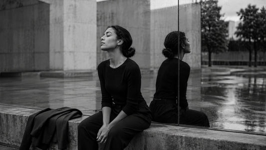 Femme assise face à son reflet dans un espace urbain en noir et blanc, symbole de la fatigue du personnage et du retour à soi Mindset Ambition