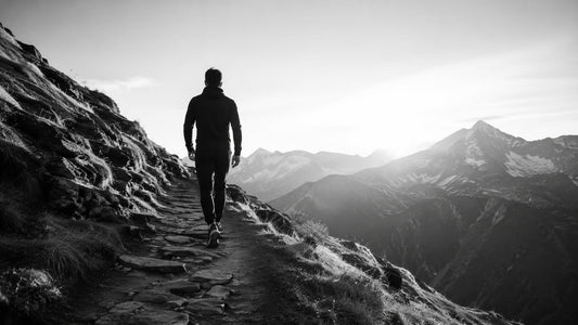 Homme marchant sur un sentier de montagne en noir et blanc, symbole du goût du difficile, de l’effort choisi et de l’élévation personnelle Mindset Ambition