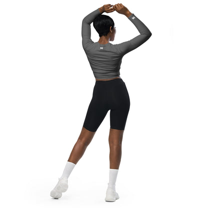 T-shirt sport femme Evolve Mindset Ambition, gris, crop-top à manches longues porté par une femme de dos, bras levés, logo blanc centré en haut du dos et sur le poignet droit.