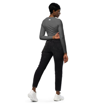 T-shirt sport femme Evolve Mindset Ambition, gris, crop-top à manches longues porté par une femme de dos avec un jean noir, logo blanc centré en haut du dos et sur le poignet droit.